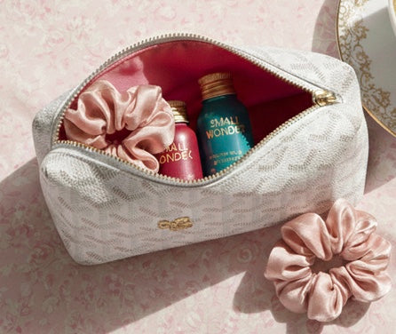 Opened travel toiletry bag on a hotel bathroom counter with small-format hair care bottles visible next to a scrunchie