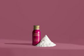 Small bottle of Small Wonder Signature shampoo with a pile of white powder on a pink background